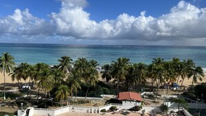 Une vue sur la plage, avec des palmiers, une zone délimitée par une clôture et un bâtiment doté d’un toit rouge.