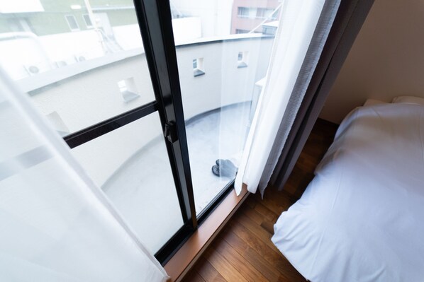 A hotel room with a large window, a wooden floor, and a bed with white bedding. - Satellite Hotel Roppongi (Tokyo)