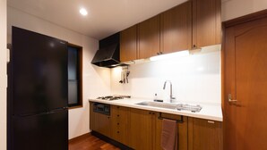 Une cuisine de taille réduite, dotée de meubles en bois, d’un réfrigérateur noir, d’une cuisinière à gaz et d’un évier.