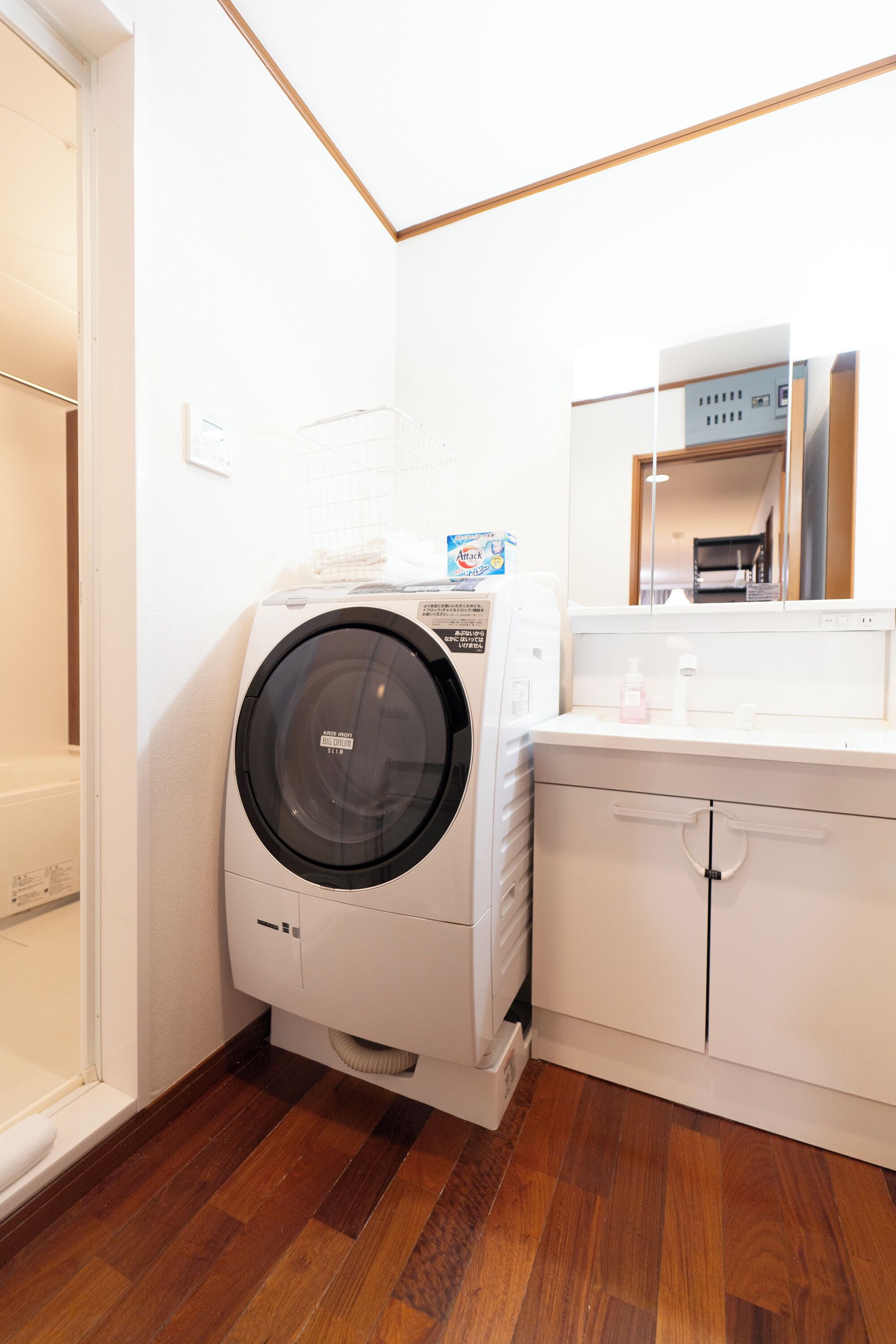 Een kleine wasruimte met een voorlader wasmachine en droger, een klein aanrecht met een spiegel, en een houten vloer.