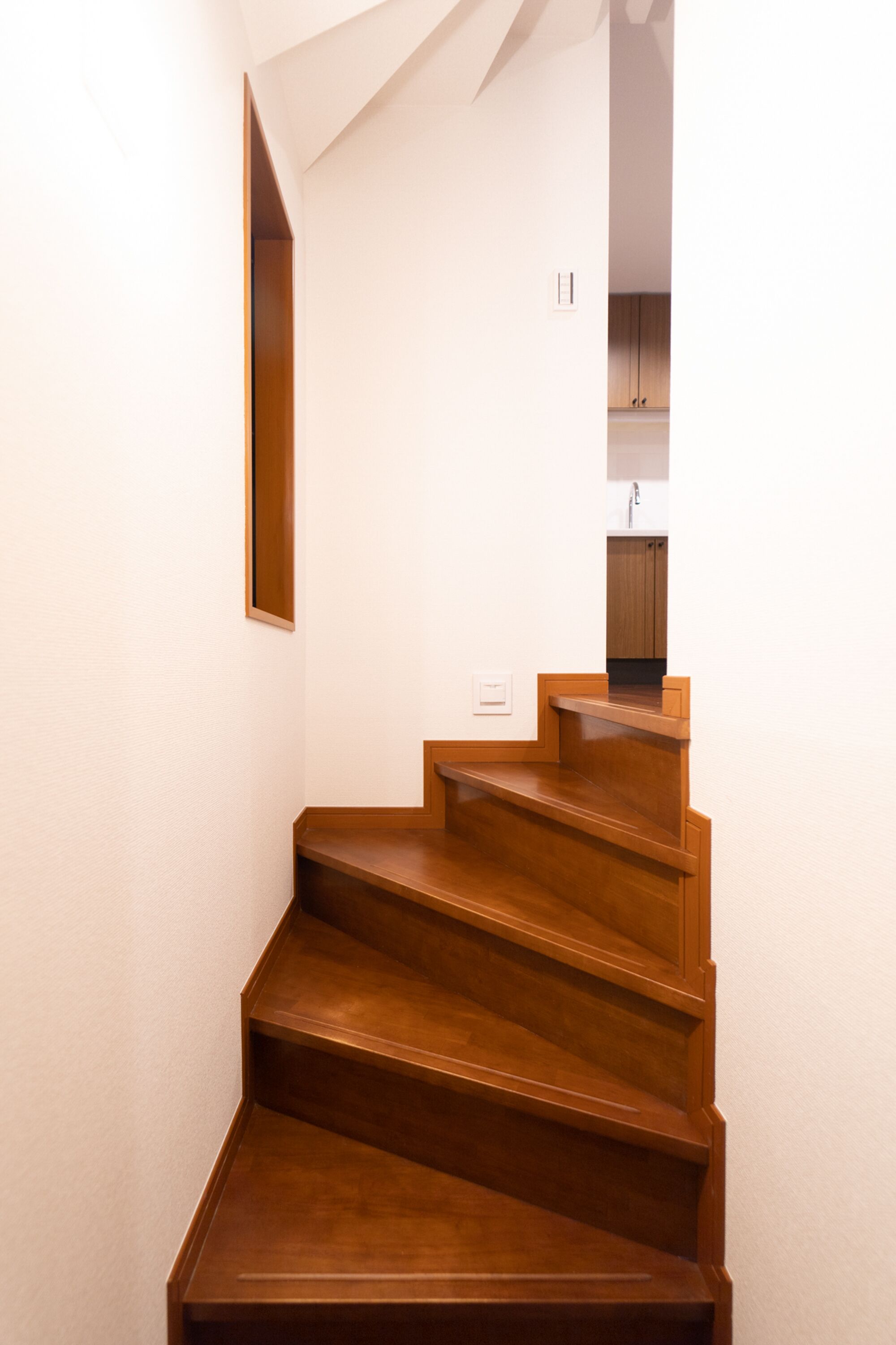 A wooden staircase leading to a kitchen area with white walls and a wooden cabinet.