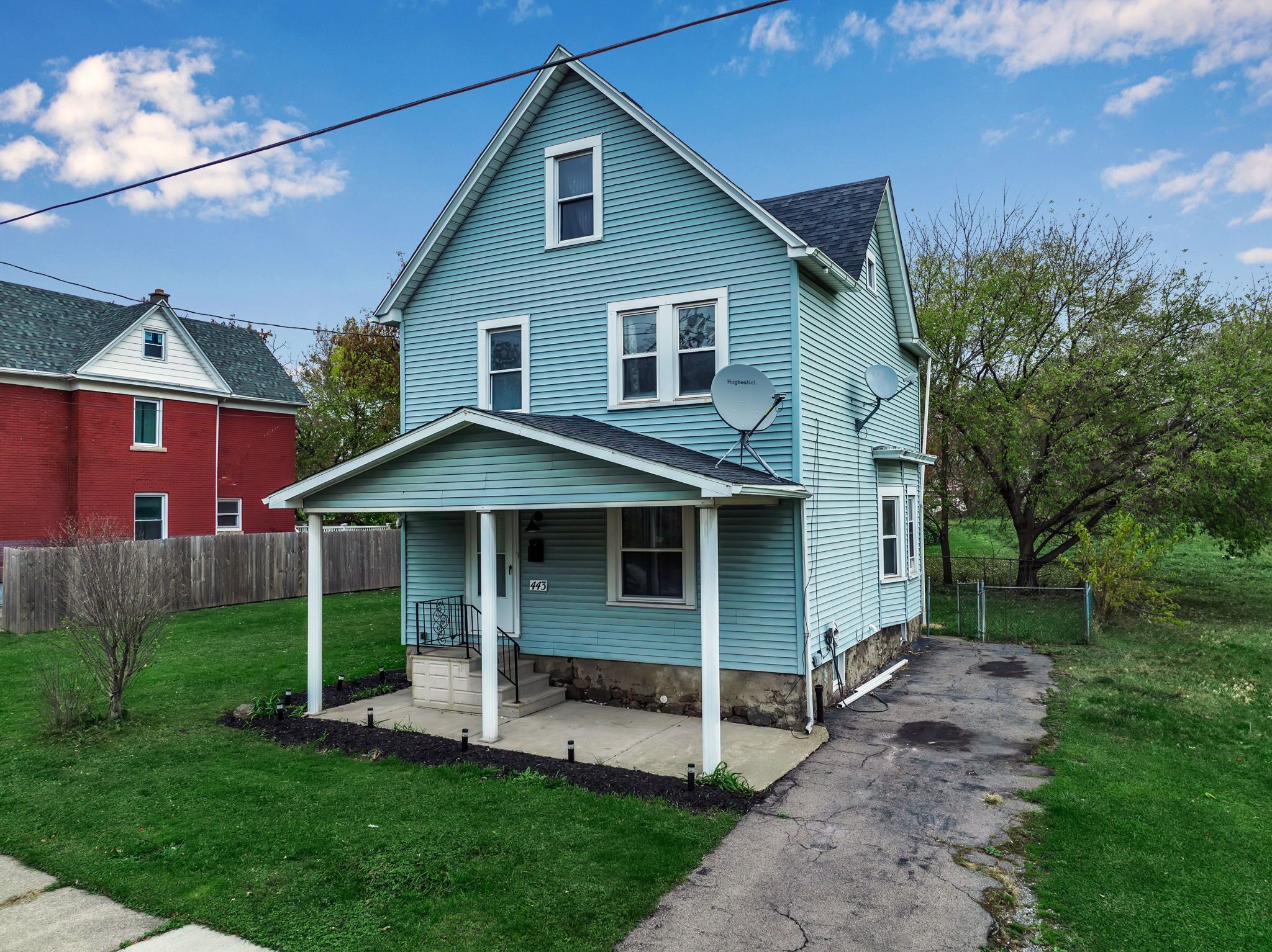 A two-story house with a porch, satellite dish, and a number '443' on the front wall.