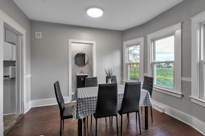 Uma sala de jantar com uma mesa posta para quatro pessoas, um espelho e vista para o exterior.