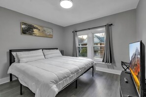 Quarto moderno com uma cama grande, televisão de tela plana e janela com cortinas.