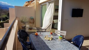 A balcony with a table, chairs, a potted plant, and a TV mounted on the wall. - Beautiful  flat with air conditioning, swimming pool and parking - 6REFC5 (SAINT CYPRIEN PLAGE)