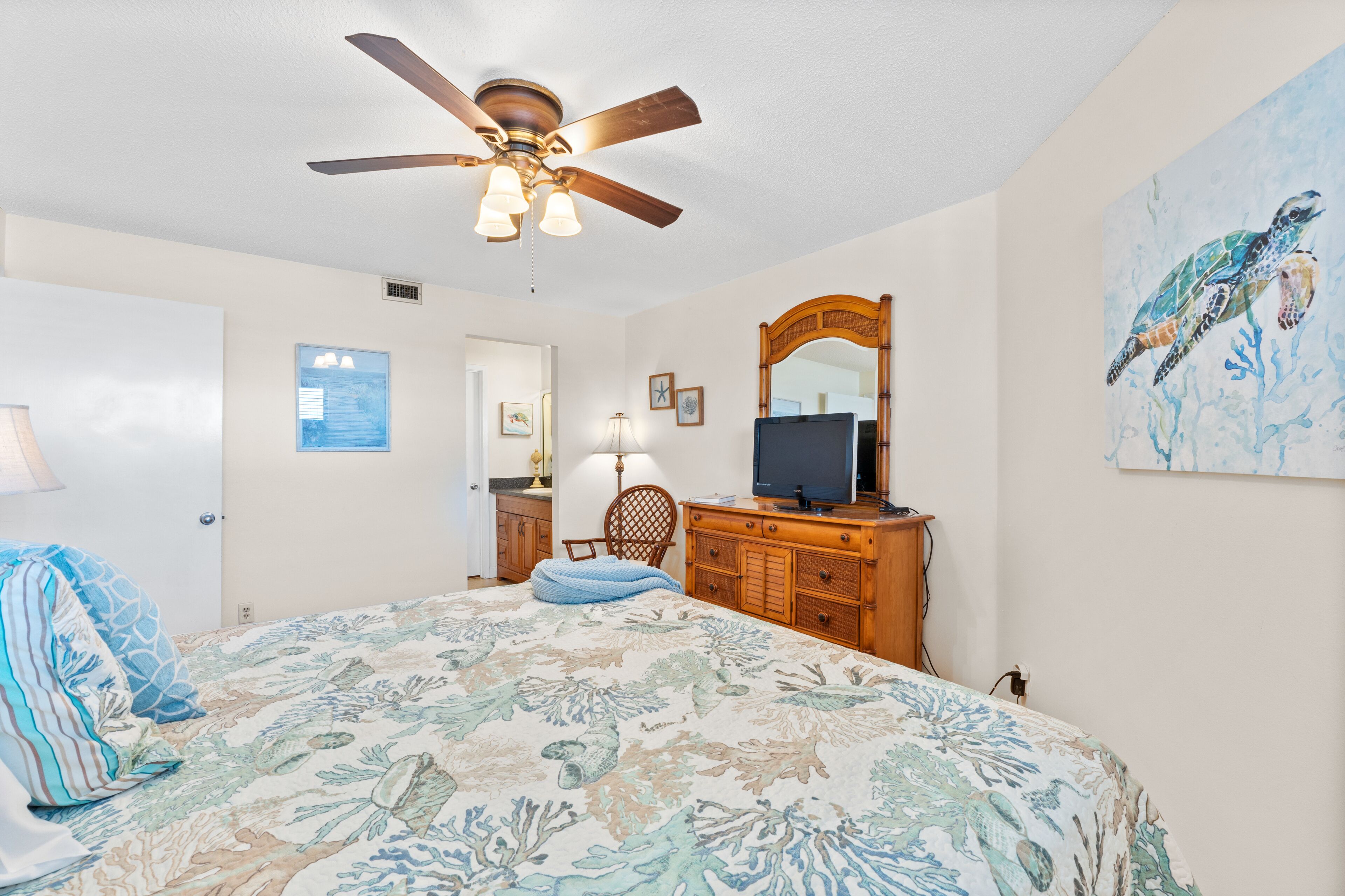 A bedroom with a bed, a ceiling fan, a dresser, a TV, and artwork on the walls.