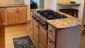 Una cocina con armarios de madera, una isla central con estufa y un tapete estampado.