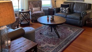 Una sala de estar con ventilador de techo, sillón estampado, sofá, mesa de centro y alfombra grande.