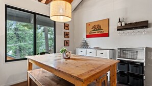 A dining area with a wooden table, a hanging light fixture, a California Republic sign, and a wine rack.