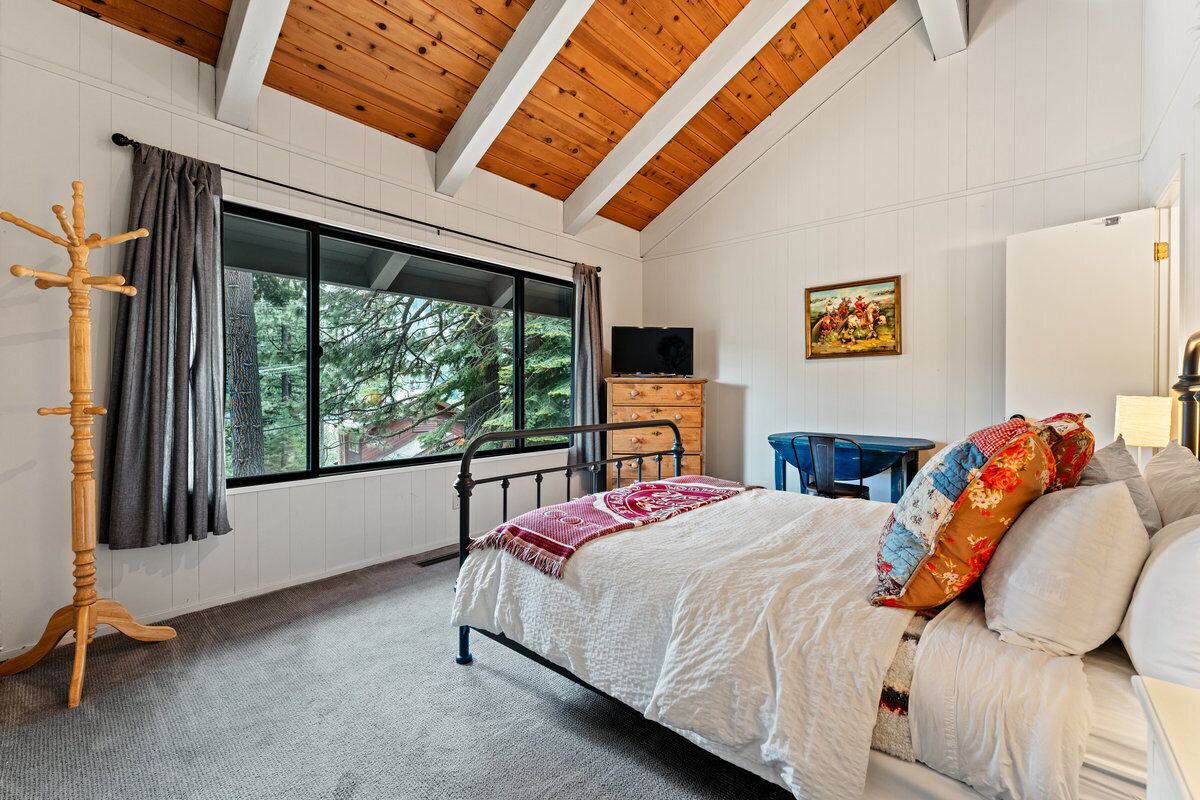 A bedroom with a bed, a wooden coat rack, a dresser, a television, and a window with a view of trees.