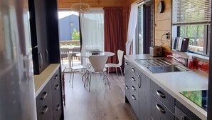 A modern kitchen with a refrigerator, stove, and sink. There is a dining area with a table and chairs. - The Bach in old Wharewaka well located for a fabulous lake holiday. (Taupo)