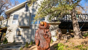 Une statue d’ours en bois se trouve devant une maison dotée d’un porche et d’un arbre.