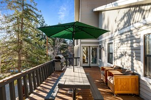 Eine Holzterrasse mit Sonnenschirm, Holzbanken und einem Grill.