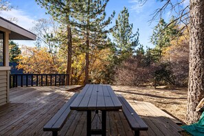 Eine Holzterrasse mit Picknicktischen, umgeben von Bäumen und einem Gebäude.