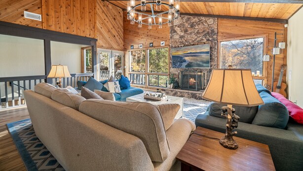 Un salon chaleureux avec une cheminée, un plafond en bois et de grandes fenêtres donnant sur l’extérieur.