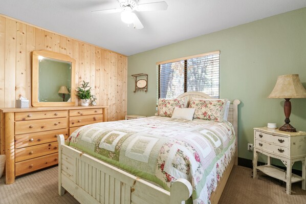 A bedroom with a wooden dresser, a bed with floral bedding, a nightstand, and a ceiling fan.