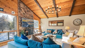 Un salon chaleureux avec un mur en pierre, un plafond en bois et une grande fenêtre. On y trouve un canapé bleu, un canapé blanc et une table basse.