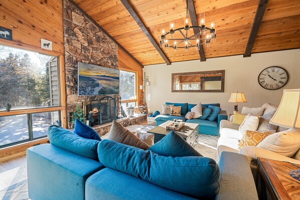 Ein gemütliches Wohnzimmer mit Steinwand, Holzboden und einem großen Fenster. Es gibt ein blaues Sofa, ein weißes Sofa und einen Couchtisch.