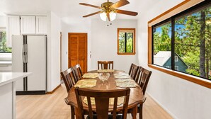 A dining area with a wooden table and chairs, a ceiling fan, and a window with a view of trees.