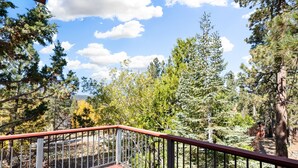 A wooden deck with a metal railing overlooking a forested area with various trees and a clear sky. - Silver Rays - Walk to Lake/Village, Game Room, Pool Table, Air Hockey, BBQ (Big Bear Lake)