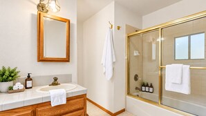 A bathroom with a wooden vanity, a large mirror, a glass-enclosed shower, and a potted plant.