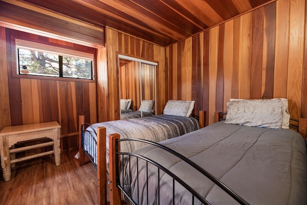A wooden-paneled room with two beds, a small table, and a window. - Silver Rays - Walk to Lake/Village, Game Room, Pool Table, Air Hockey, BBQ (Big Bear Lake)