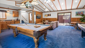 A pool table in a room with wooden beams and a blue carpet. There is a sofa and a dining table with chairs. - Silver Rays - Walk to Lake/Village, Game Room, Pool Table, Air Hockey, BBQ (Big Bear Lake)