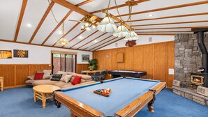 A room with a pool table, wooden ceiling beams, and a stone fireplace.