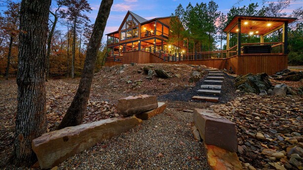 A large wooden cabin with multiple levels, a covered porch, and a stone pathway leading to the entrance. - Creekside 6BR Retreat w/ UTV Trails & Hot Tub & Pet-Friendly (Broken Bow)