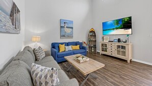 Un salon avec un canapé bleu, une table basse en bois, un téléviseur et une bibliothèque.