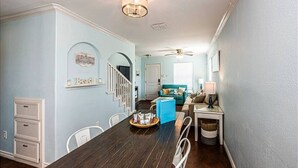 Un espace repas comprenant une longue table, des chaises, un canapé bleu et un ventilateur de plafond.
