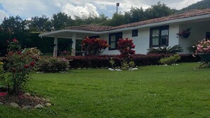 A house with a white exterior and a tiled roof, surrounded by a well-maintained garden with various plants and flowers. - Marina Private Villa (Zarzal)