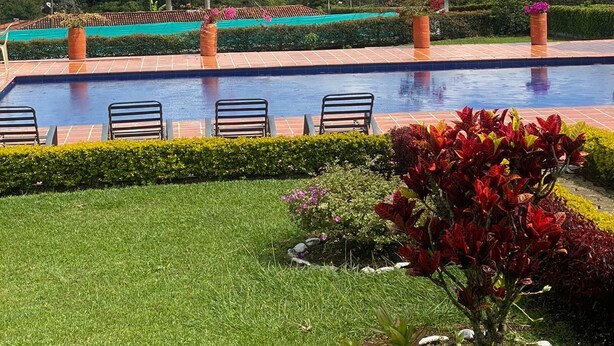 A swimming pool with lounge chairs, surrounded by well-maintained gardens and a view of a lake and hills. - Marina Private Villa (Zarzal)