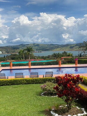 A swimming pool with lounge chairs, surrounded by well-maintained gardens and a view of a lake and hills. - Marina Private Villa (Zarzal)