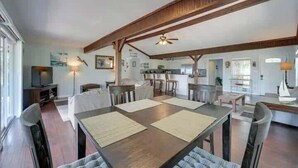 Un vaste espace dédié à la salle à manger, avec une grande table en bois, de nombreuses chaises et un ventilateur de plafond.