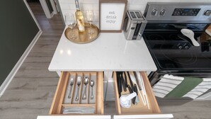 A kitchen with a built-in wine cooler, a framed sign saying "eat drink enjoy," and a drawer with utensils.