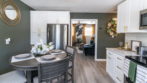 A modern kitchen with white cabinets, a stainless steel refrigerator, and a dining area with a round table and chairs.