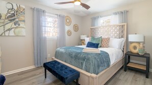 A bedroom with a bed, a bench, a ceiling fan, and a bedside table with a lamp.