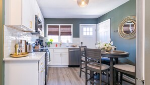 A modern kitchen with white cabinets, a dining area with a table and chairs, and a large window with blinds.