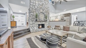 A modern living room with a stone fireplace, a ceiling fan, and a kitchen in the background. - Beautiful Lake getaway with pool, upgraded, pet friendly with lots of extras!! (Green Cove Springs)