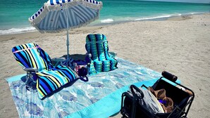 A beach setup with striped beach chairs, a blue and white striped umbrella, and a beach bag on a towel. - Luxury Condo at River Strand Golf & Country Club - 2027 Available! (Bradenton)