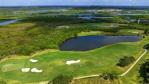 An aerial view of a golf course with multiple ponds, sand bunkers, and a clear sky. - Luxury Condo at River Strand Golf & Country Club - 2027 Available! (Bradenton)