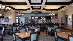 A spacious restaurant with multiple tables and chairs, a bar area, and a ceiling with recessed lighting and chandeliers. - Luxury Condo at River Strand Golf & Country Club - 2027 Available! (Bradenton)