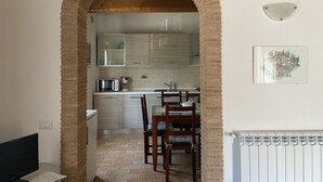Cozinha com arco de tijolos, armários brancos e área de refeições com cadeiras de madeira.