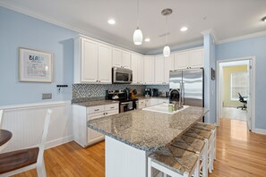 Una cocina moderna con armarios blancos, encimeras de granito, electrodomésticos de acero inoxidable y una zona de bar con taburetes.