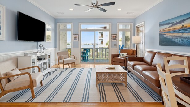 A spacious living room with a large TV, comfortable seating, a ceiling fan, and a view to the outside. - 20 Turtle Bay! 30 Night Minimum Stay - River View, Community Pool & Dock (Folly Beach)
