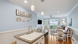 A kitchen with a granite countertop, white cabinetry, and a built-in dishwasher. There is a dining area with a table and chairs, and a large window offering a view. - 20 Turtle Bay! 30 Night Minimum Stay - River View, Community Pool & Dock (Folly Beach)