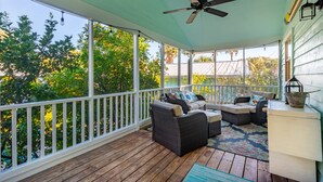 A covered porch with wicker furniture, a ceiling fan, and a view of trees and a house.