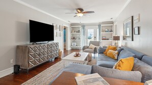 A modern living room with a flat-screen TV, a ceiling fan, and a sofa with cushions.