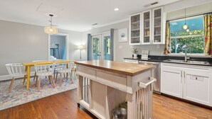 A modern kitchen with white cabinets, a wooden island, and a dining area with a table and chairs.